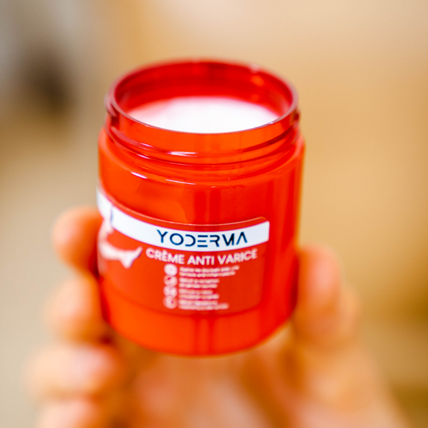 Une main tient le pot de crème yoderma une crème naturelle qui lutte efficacement contre les varices et les jambes lourdes 